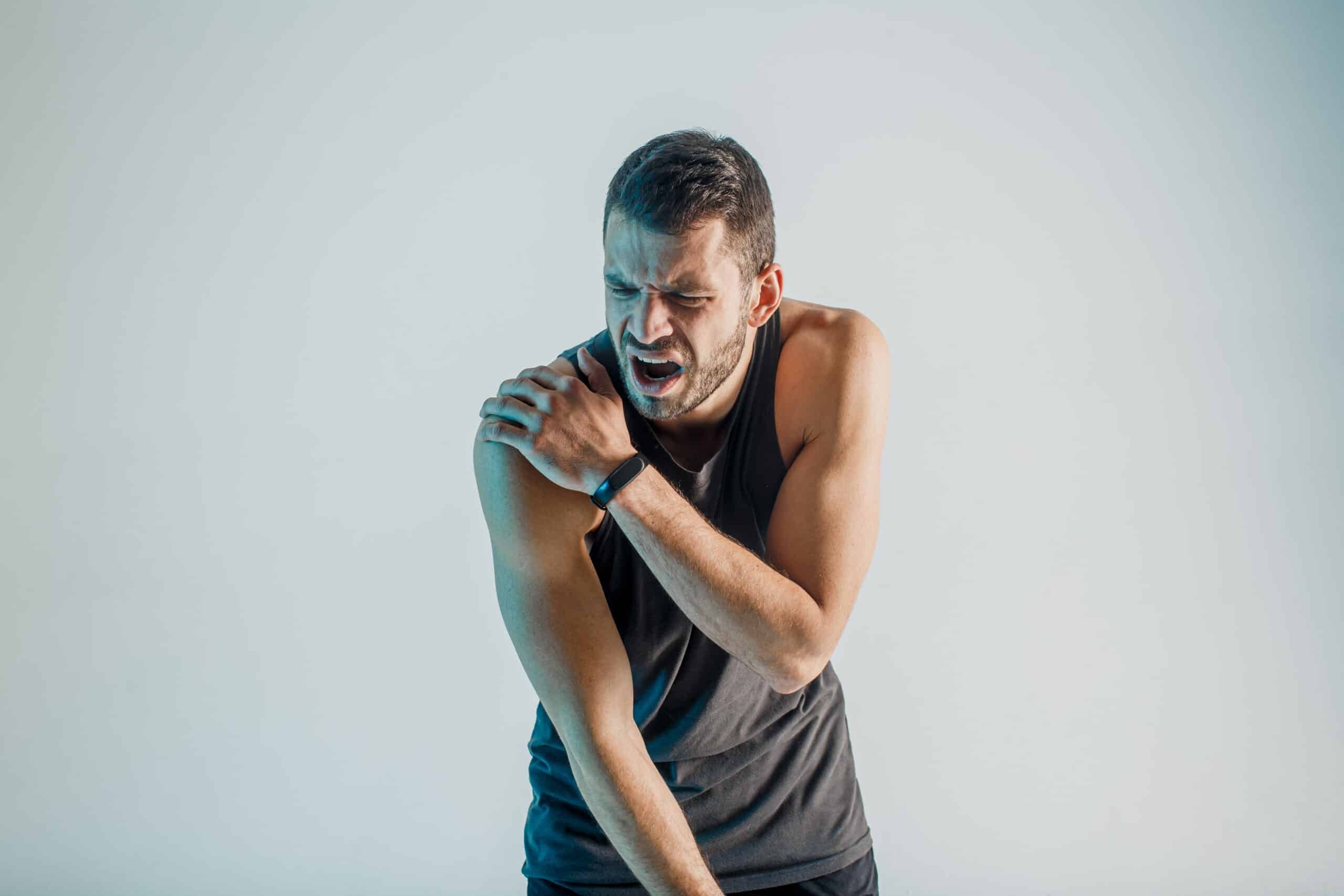 Exhausted sportsman feeling pain in shoulder. Young bearded european man wear sports uniform. Concept of sports injury. Isolated on turquoise background. Studio shoot. Copy space
